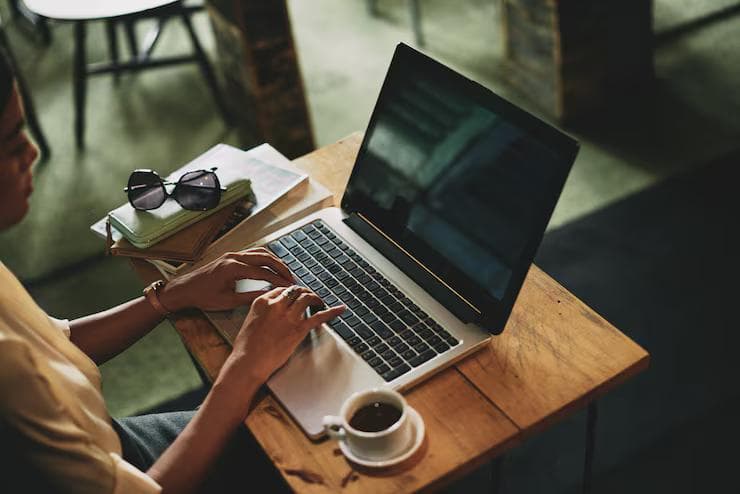 A woman looks at her monitor and laptop intently.
